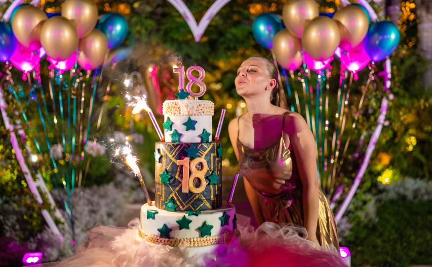 A girl is celebrating her birthday with a large cake at her birthday party in a vibrant and well-decorated venue