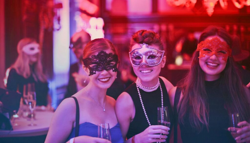 Three female are smiling wearing masks that represent the birthday party theme