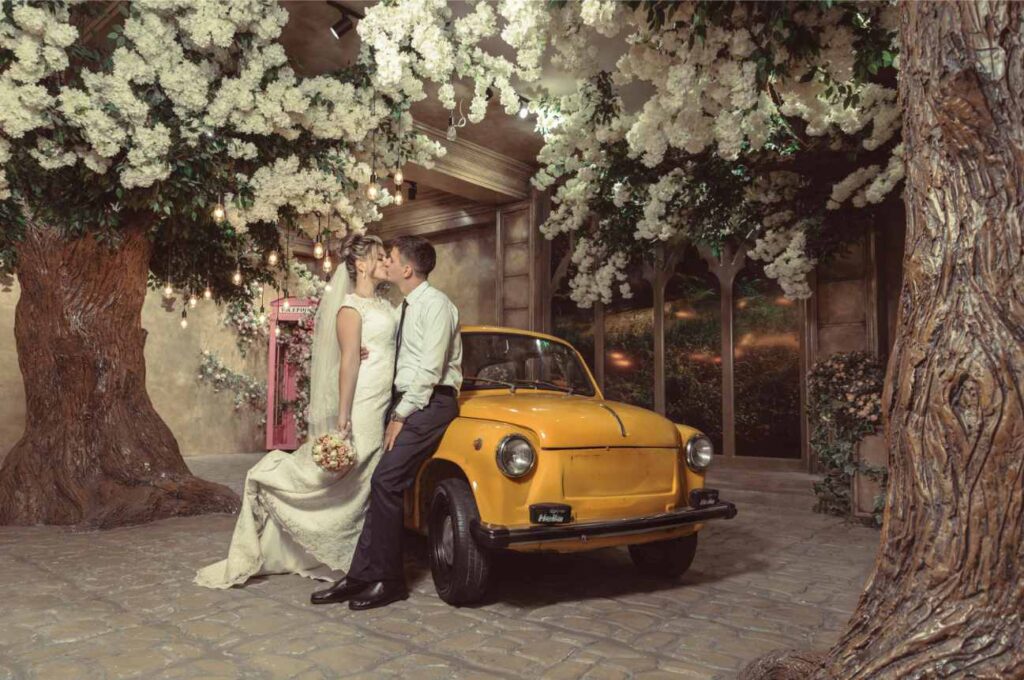 Ending of a wedding ceremony where bride and groom kissing each other in front of a vintage car - How Long Do Weddings Last?